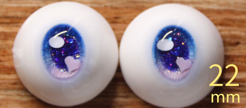 May include: A pair of blue and white doll eyes with glitter and white hearts. The eyes are 22 mm in diameter.