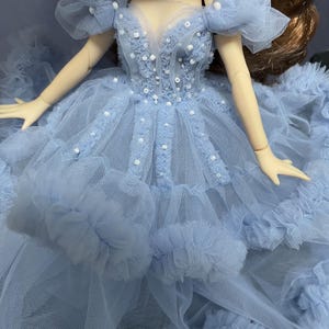 May include: A light blue tulle dress with a sweetheart neckline and beaded embellishments. The dress has a layered skirt with ruffles.