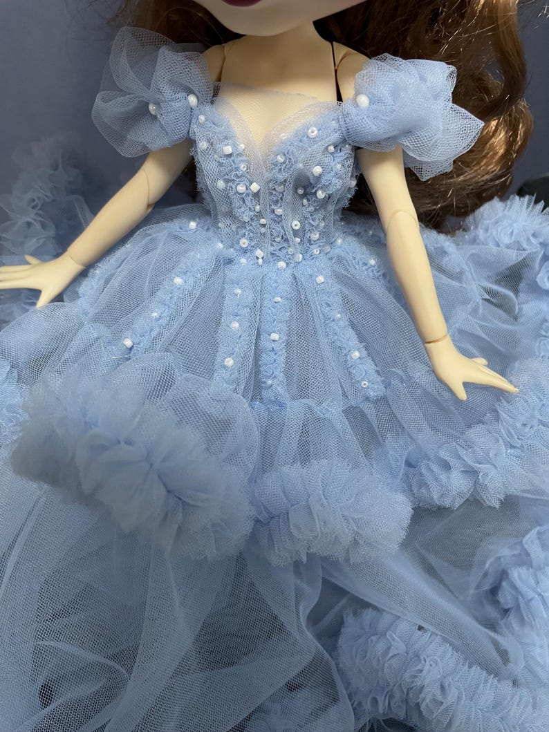 May include: A light blue tulle dress with a sweetheart neckline and beaded embellishments. The dress has a layered skirt with ruffles.