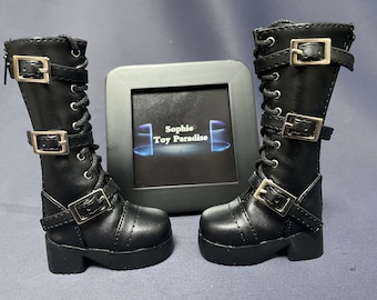 May include: A pair of black leather boots with silver buckles and laces. The boots have a chunky heel and a platform sole. The boots are on a gray surface.