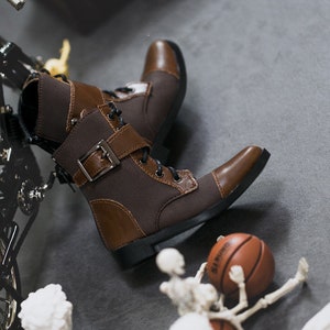 May include: Brown leather ankle boots with laces and a buckle. The boots have a brown canvas panel and a black sole.