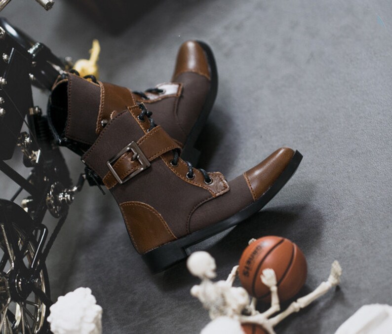 May include: Brown leather ankle boots with laces and a buckle. The boots have a brown canvas panel and a black sole.
