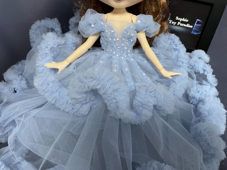 May include: A light blue tulle dress with a ruffled skirt and beaded bodice. The dress is designed for a doll.