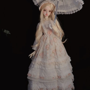 May include: A porcelain doll wearing a white dress with floral print and lace trim. The doll is holding a white lace parasol with a silver handle.