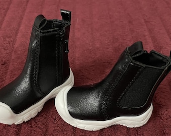 May include: A pair of black leather ankle boots with white soles. The boots have a zipper on the side and a pull tab on the back.