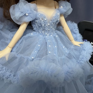 May include: A light blue tulle dress with a sweetheart neckline and pearl embellishments. The dress has a ruffled skirt and a large flower on each shoulder.