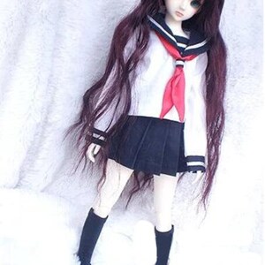 May include: A doll wearing a white sailor shirt with a red tie, a black skirt, and black socks. The doll has long, dark brown hair and blue eyes.