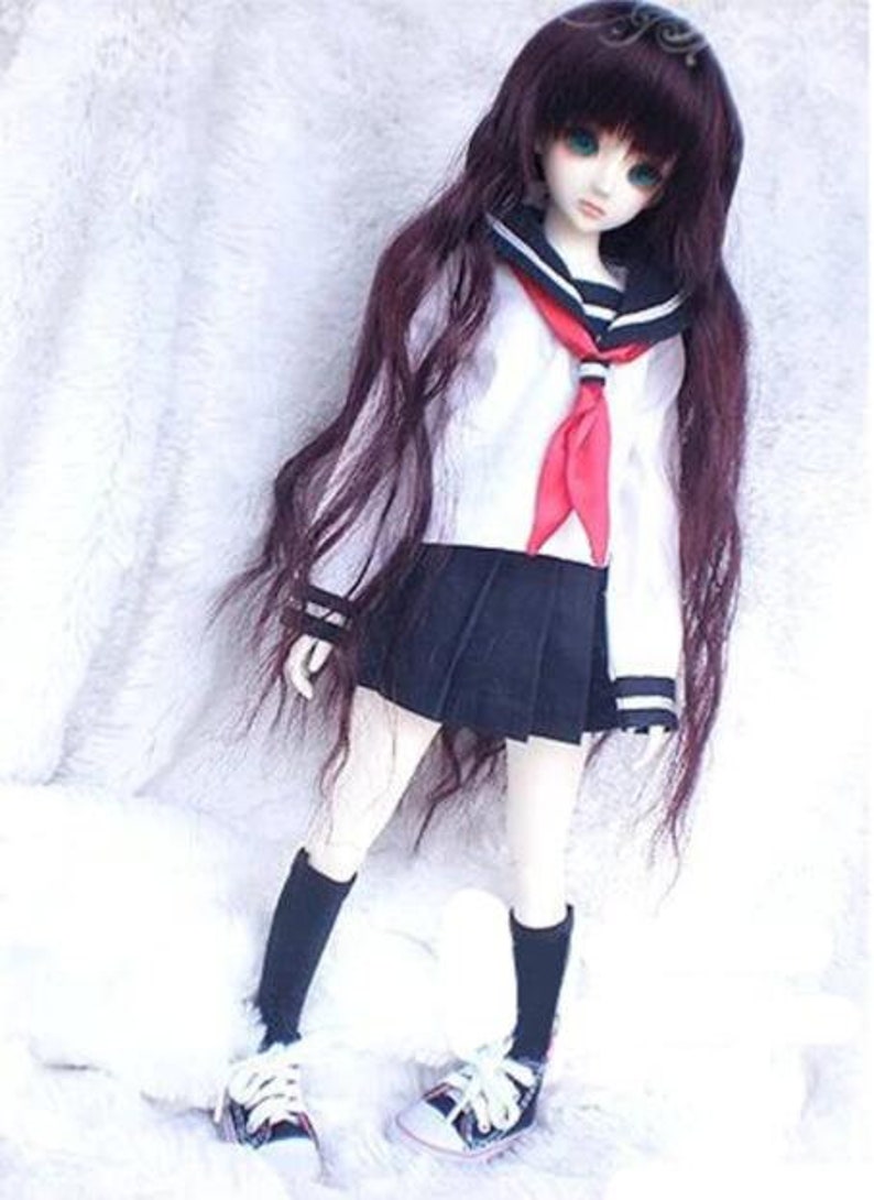 May include: A doll wearing a white sailor shirt with a red tie, a black skirt, and black socks. The doll has long, dark brown hair and blue eyes.