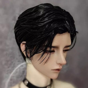 May include: A doll's head with black, slicked-back hair. The doll has pale skin, delicate features, and closed eyes. It wears a black choker with a silver stud. The background is a blurred grey.