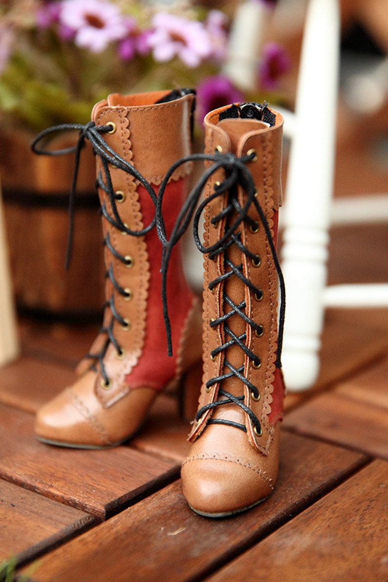 May include: A pair of brown and red lace-up boots with a scalloped edge design. The boots have a pointed toe and a small heel. Black laces are threaded through brass eyelets. The boots are made of leather and have a vintage aesthetic.