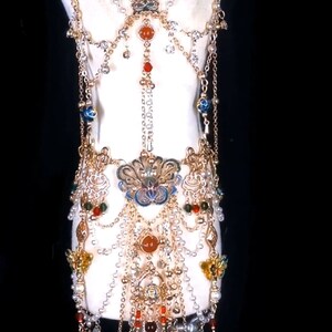 May include: A gold and silver body chain with multiple layers of beads and charms. The chain features a large, ornate pendant with blue and gold enamel. The beads are red, orange, green, and white.