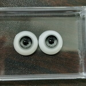 May include: Two gray and white doll eyes with black pupils. The eyes are in a clear plastic container.