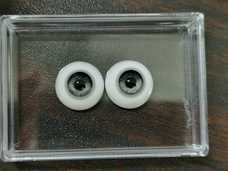 May include: Two gray and white doll eyes with black pupils. The eyes are in a clear plastic container.