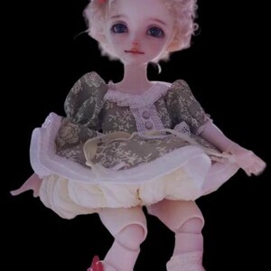 May include: A doll with a pale complexion, blue eyes, and curly blonde hair. The doll wears a green and white dress with a matching hat adorned with red accents. The doll's outfit includes white lace socks and a red bow.
