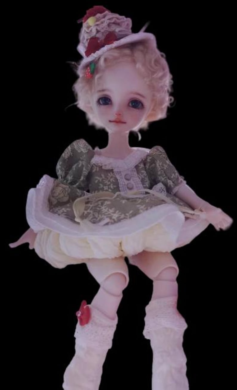 May include: A doll with a pale complexion, blue eyes, and curly blonde hair. The doll wears a green and white dress with a matching hat adorned with red accents. The doll's outfit includes white lace socks and a red bow.