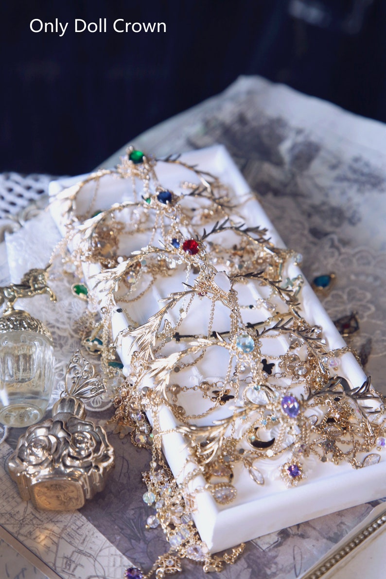 May include: A collection of gold-toned metal doll crowns featuring intricate branch-like designs, delicate chains, and various colorful faceted gemstones including red, blue, green, and purple. The text Only Doll Crown is visible at the top left.