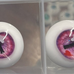 May include: Two white doll eyes with a purple and pink iris, a black pupil, and white and red accents.