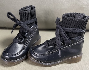 May include: A pair of black leather ankle boots with black knit cuffs and laces. The boots have a round toe and a chunky sole.