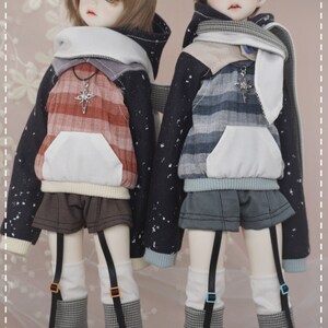 May include: Two dolls wearing black and white patterned hoodies with white collars and matching black and white checkered leggings. The doll on the left is wearing a red and white plaid shirt underneath the hoodie and the doll on the right is wearing a blue and white plaid shirt underneath the hoodie.