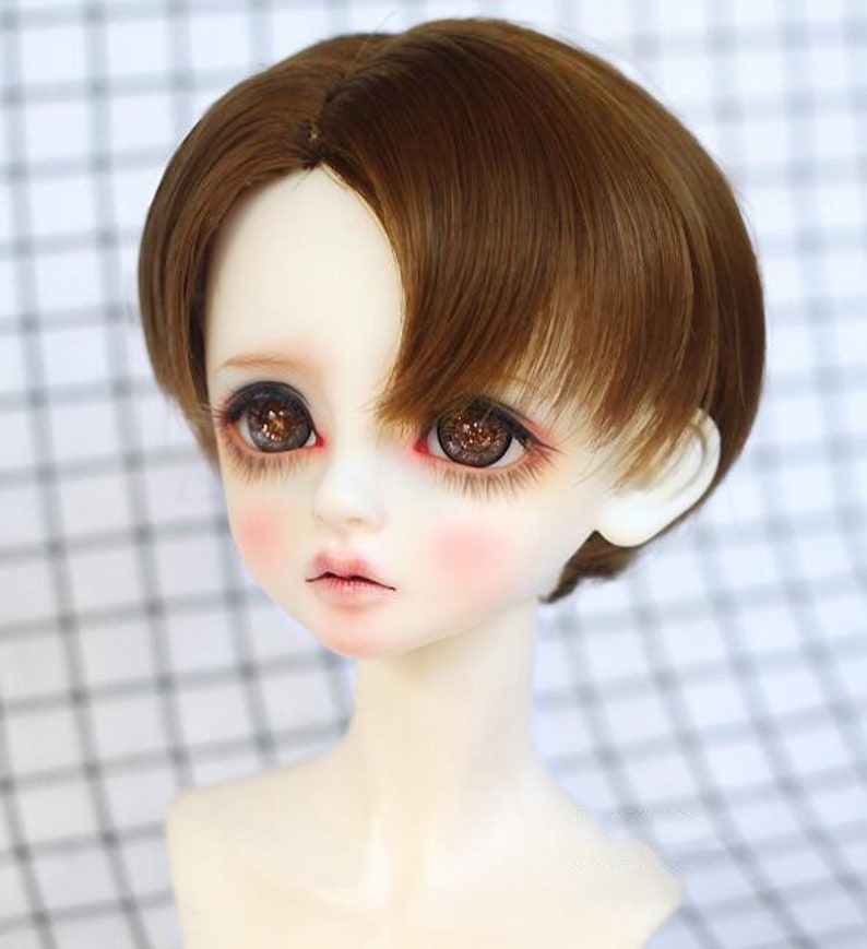 May include: A brown wig with a side part and short bangs. The wig is styled in a boyish cut and is made of synthetic hair.