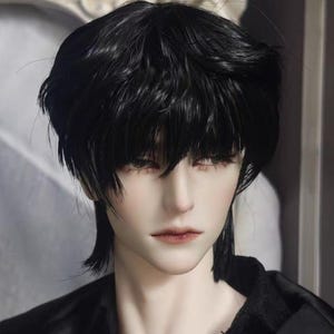 May include: A doll head featuring short, layered black hair with a textured, piecey fringe that falls over the forehead. The doll has pale skin, defined facial features, dark eyelashes, and soft, neutral-toned lips, wearing a black collared shirt.