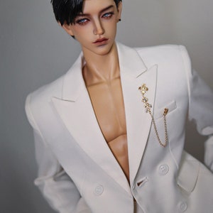 May include: A white double-breasted blazer with a gold chain and a decorative pin. The blazer has a sharp, tailored look.