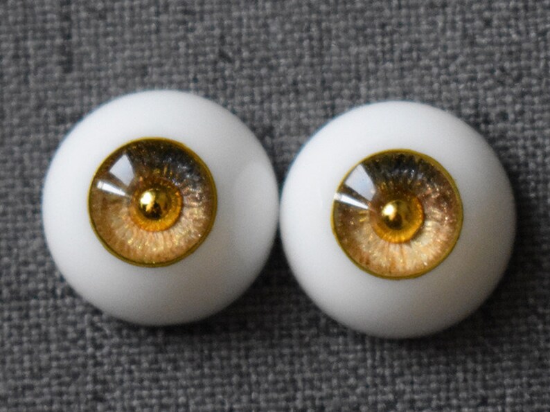 Puede incluir: Dos ojos de mu&ntilde;eca marrones y dorados con escler&oacute;tica blanca e iris dorado. Los ojos tienen un acabado brillante.