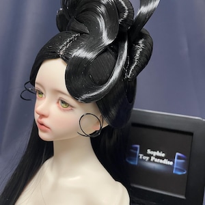 May include: A doll with pale skin, green eyes, and black hair styled in an elaborate updo. The doll wears black hoop earrings. The text "Sophie Toy Paradise" is visible on a black frame.