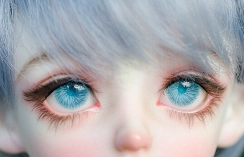 K&ouml;nnte beinhalten: Nahaufnahme eines Puppenkopfes mit blauen Augen und hellblauem Haar. Die Augen der Puppe sind offen und schauen direkt in die Kamera.
