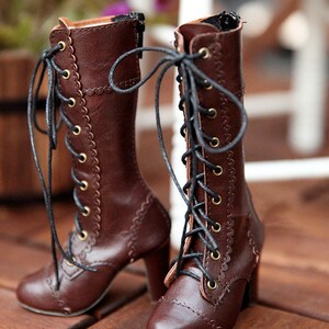 May include: A pair of brown leather boots with laces and a high heel. The boots have a scalloped edge design along the sides and gold-coloured eyelets. The laces are black, and the boots are on a wooden surface.