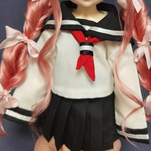 May include: A doll wearing a white sailor uniform with a black skirt, red tie, and white trim. The doll has long pink hair with pink bows.