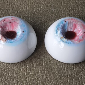 May include: Two white doll eyes with a blue, pink, and gold iris. The pupils are dark brown.
