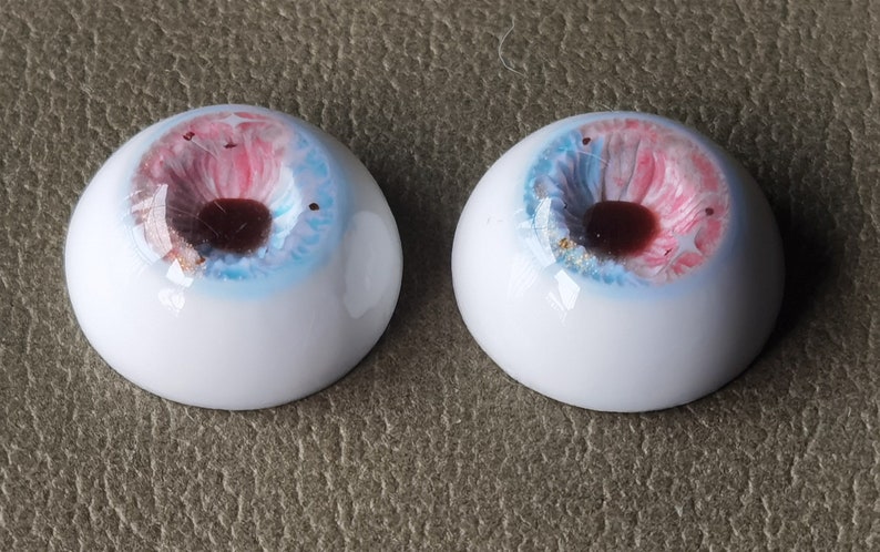 May include: Two white doll eyes with a blue, pink, and gold iris. The pupils are dark brown.