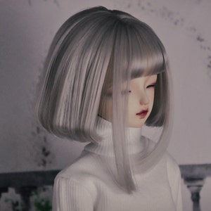May include: A doll with a short, straight, silver-grey wig with bangs. The doll is wearing a white turtleneck sweater.