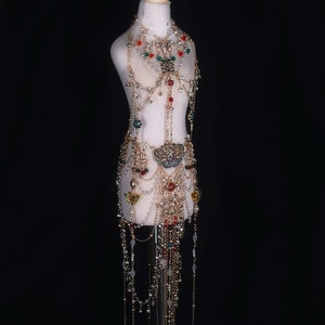 May include: A gold body chain with colorful beads and a large ornate pendant. The chain is layered with multiple strands and has a long, flowing design.