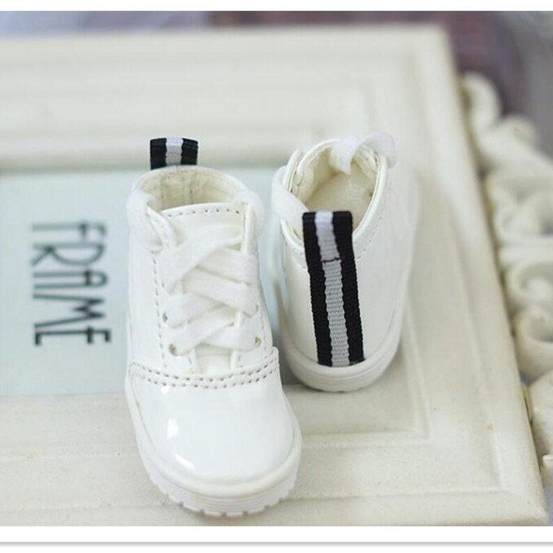 May include: A pair of white leather sneakers with black and white striped accents. The sneakers have white laces and a white rubber sole.