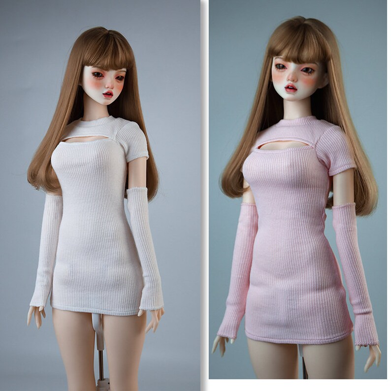 May include: Two dolls wearing different coloured ribbed knit dresses with long sleeves and a cutout at the neckline. The doll on the left is wearing a white dress and the doll on the right is wearing a pink dress.
