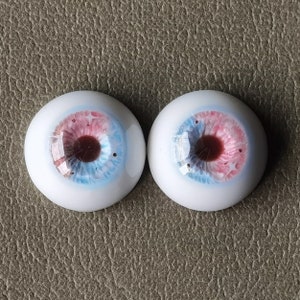 May include: Two blue, pink, and brown glass doll eyes with a white sclera.