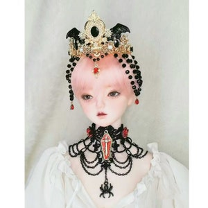 May include: A doll with pink hair wearing a black and gold crown with a black bat design and a black lace choker with a red coffin pendant and a black spider charm.