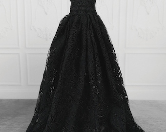 Puede incluir: Un vestido de encaje negro con cuello alto y mangas cortas. El vestido tiene un corpiño ajustado y una falda completa. El vestido está decorado con un collar de cuentas.