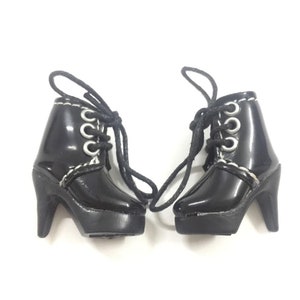 May include: A pair of black heeled boots with white stitching and silver eyelets. The boots have laces and a platform sole.