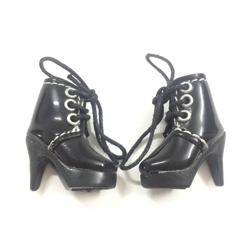 May include: A pair of black heeled boots with white stitching and silver eyelets. The boots have laces and a platform sole.
