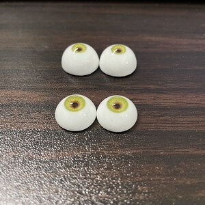 May include: Four white doll eyes with green and brown irises. The eyes are arranged in two rows of two.