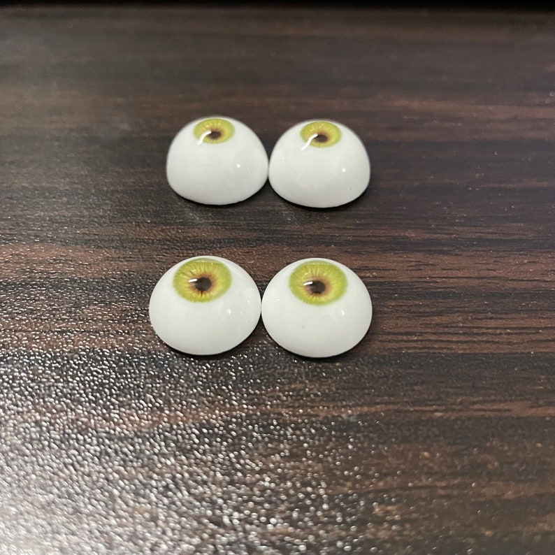 May include: Four white doll eyes with green and brown irises. The eyes are arranged in two rows of two.
