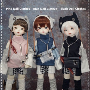 May include: Three dolls wearing different outfits. The doll on the left is wearing a pink shirt, grey pants, and a grey cat-eared hat. The doll in the middle is wearing a blue shirt, blue pants, and a grey cat-eared hat. The doll on the right is wearing a black shirt, black pants, and a black cat-eared hat. All three dolls are wearing white socks and sneakers.