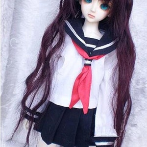 May include: A doll wearing a white sailor uniform with a red tie and a black pleated skirt. The doll has long, dark brown hair and blue eyes.