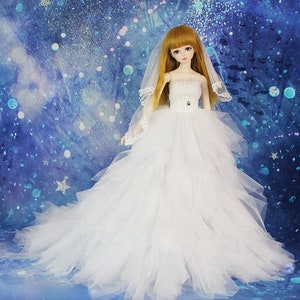 May include: A white bridal gown with a tulle skirt and a lace bodice. The doll is wearing a white veil and has long blonde hair.