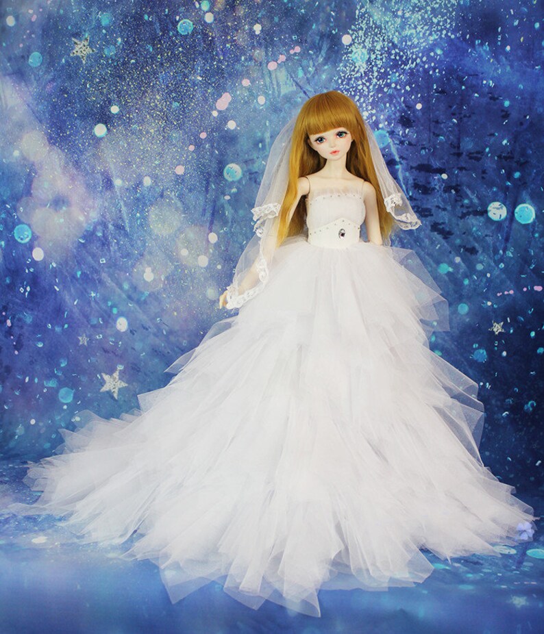 May include: A white bridal gown with a tulle skirt and a lace bodice. The doll is wearing a white veil and has long blonde hair.