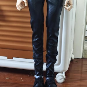 May include: Black faux leather trousers with a textured pattern and black lace-up boots. The boots have a thick sole. The doll is wearing a black top and white shirt.