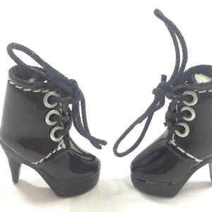 May include: A pair of black heeled boots with white stitching and silver eyelets. The boots have laces that tie at the top.